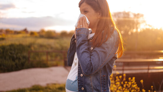 Pregnant woman sneezes and wipes her nose with a napkin while walking in the spring park.