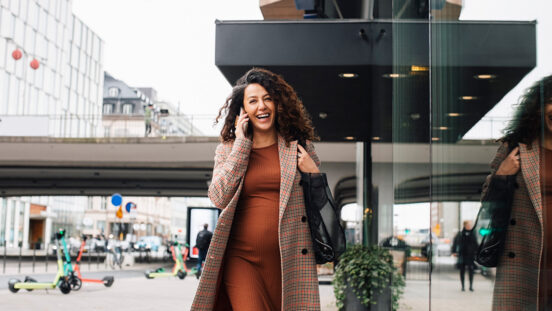 Happy female entrepreneur talking on smart phone while walking in city