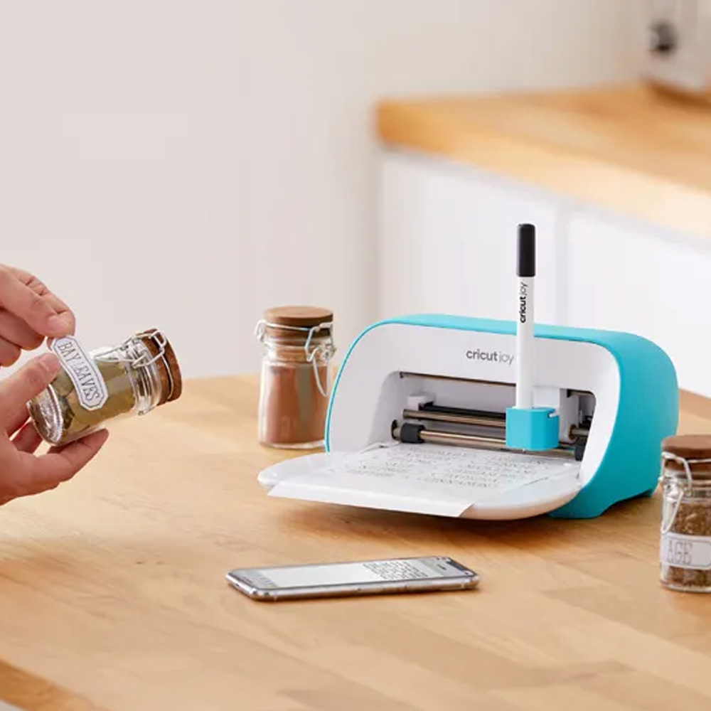 Kitchen bench with Cricut machine and jars being labelled