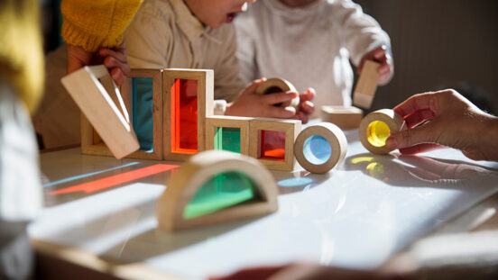 Little kids playing with colourful wooden building blocks on the table - stock photo