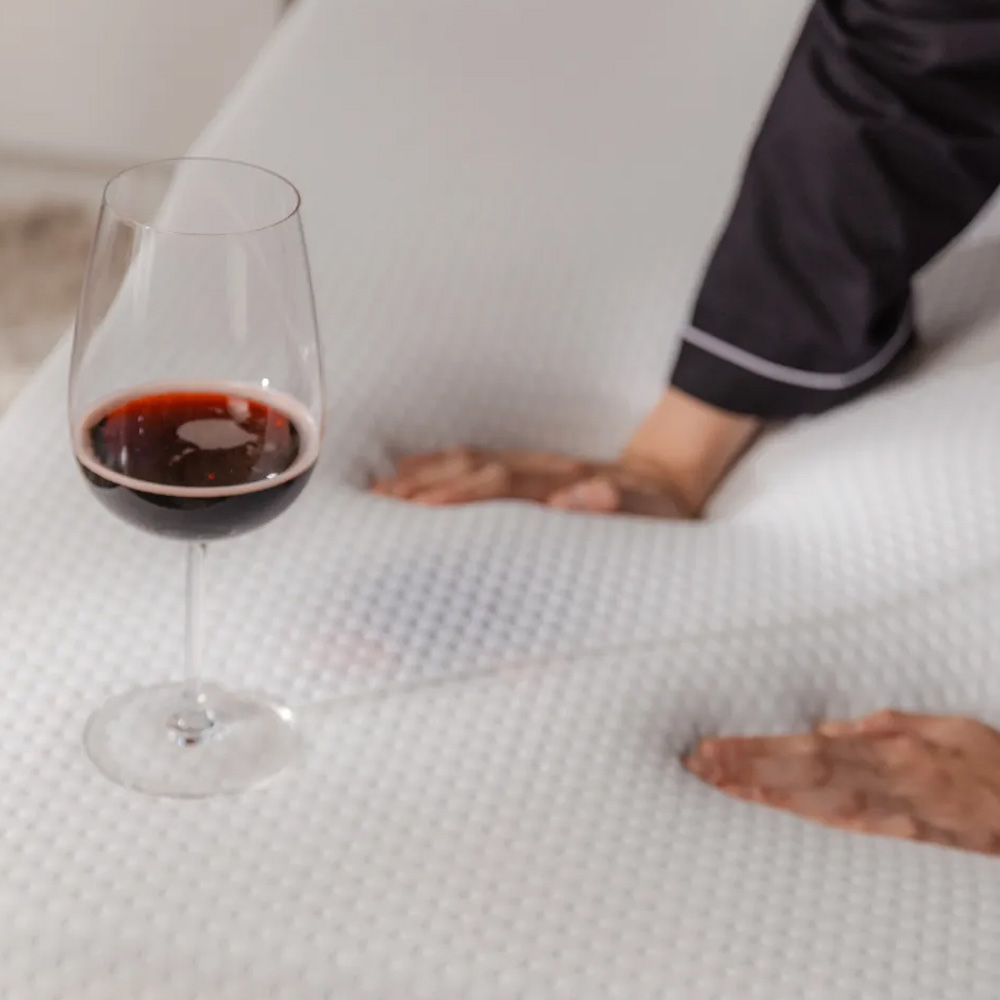 Hands demonstrating mattress stability on Emma mattress as a glass of red wine does not spill.