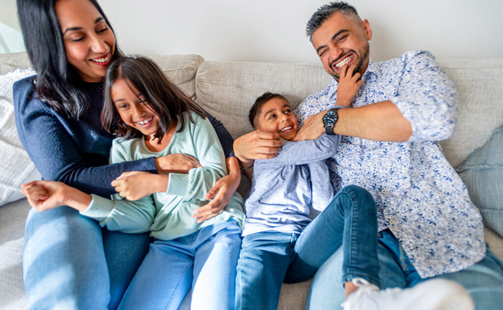 Family having fun at home playing on the sofa. There is a boy and a girl child and 2 parents. They are happy, smiling and laughing
