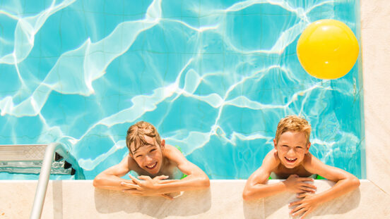 Two boys playing in swimming pool looking up to smile into camera