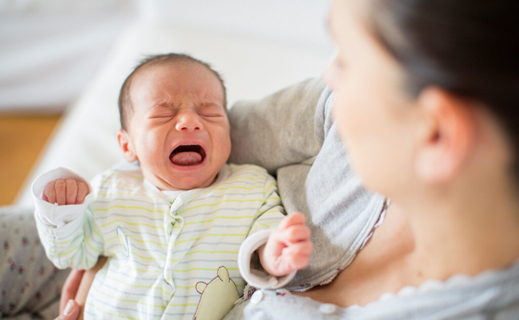 Newborn child in lime green onesie crying