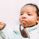 Newborn baby girl lying on bed sticking out tongue