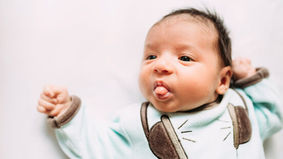 Newborn baby girl lying on bed sticking out tongue