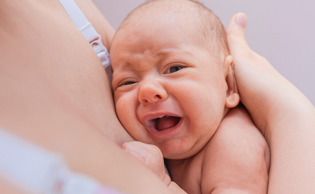 Baby crying on mother's breast close-up