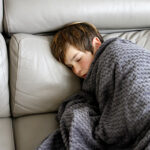 Boy with cold and flu covered with blanket on sofa