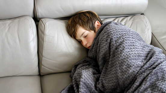 Boy with cold and flu covered with blanket on sofa