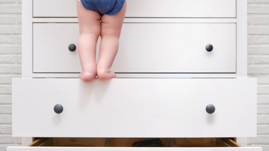 Chubby bare legs of toddler using open drawers like steps to climb up a piece of furniture