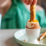 Close up image of a child dipping a finger of toast into a soft boiled egg, which contains zinc