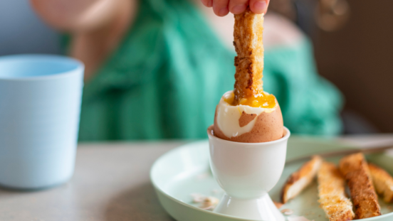 Close up image of a child dipping a finger of toast into a soft boiled egg, which contains zinc