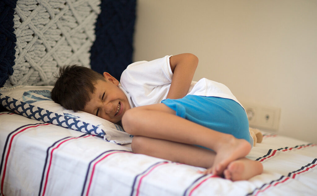 Young boy lying in bed with stomachache