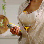 Medela Freestyle™ Hands-Free Breast Pump lifestyle image of woman in beige blouse using pump in modern home