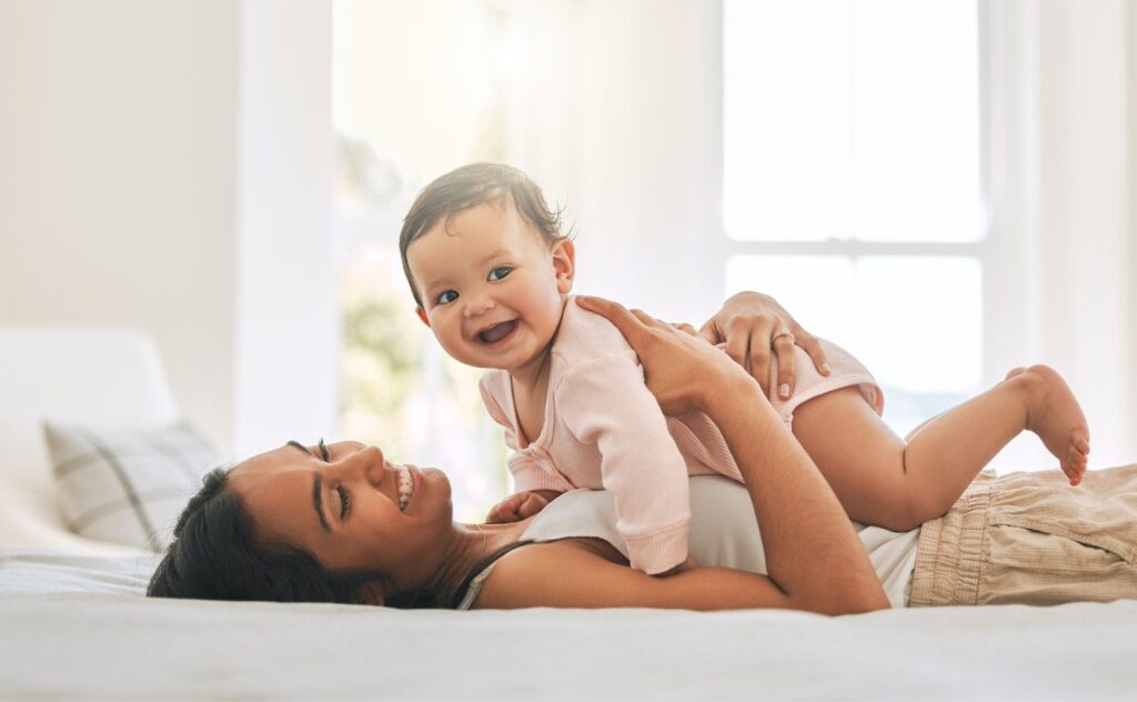 Young woman lying on bed with smiling baby