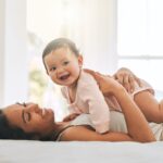 Young woman lying on bed with smiling baby