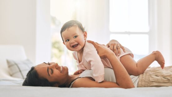 Young woman lying on bed with smiling baby