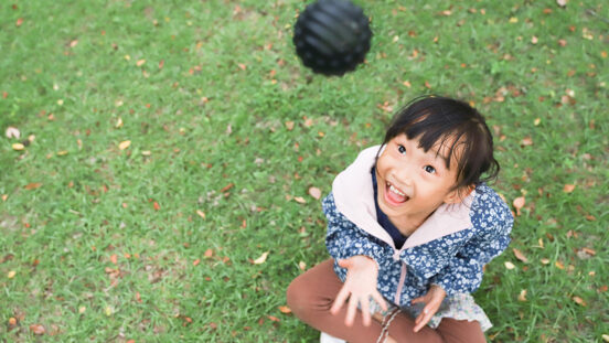 An Asian girl is playing with a ball on the grass, she throws the ball up and practices catching it.