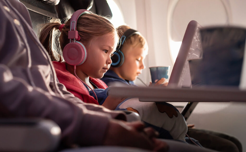 Cute little girl and boy using digital tablet while flying on an airplane.