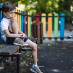 Primary school aged boy looking sad as he sits alone in a colourful playground