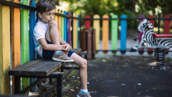 Primary school aged boy looking sad as he sits alone in a colourful playground