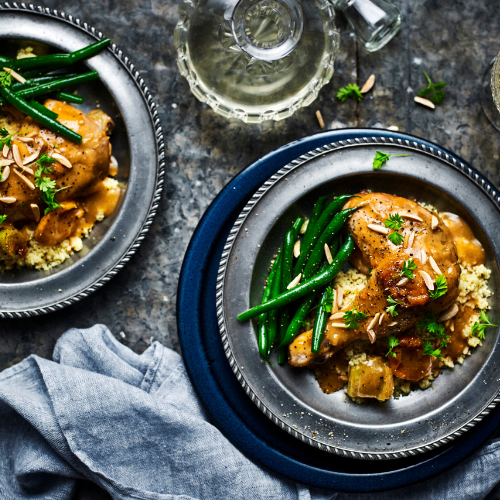 Aerial view of a dark table set with two plates of slow cooker apricot chicken with green neans and potatoes