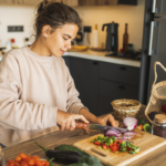 Young olive-skinned woman chopping up a variety of vegetables in a warmly lit kitchen