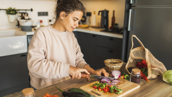 Young olive-skinned woman chopping up a variety of vegetables in a warmly lit kitchen