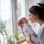 Loving and affectionate mother holding newborn baby indoors at home.