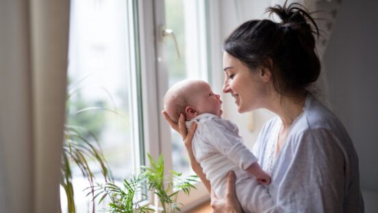 Loving and affectionate mother holding newborn baby indoors at home.