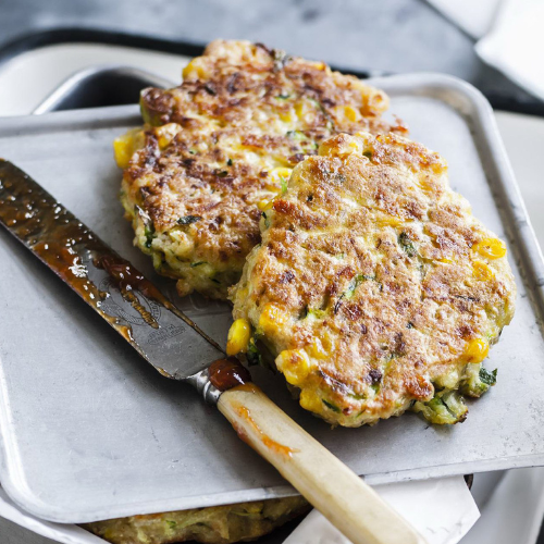 Serving of twp corn, zucchini and chickpea fritters with a knife with chutney on the blade