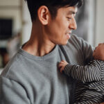 Smiling Asian father shot holding his baby daughter looking at each other. Happy family portrait. Father sharing parental responsibility.