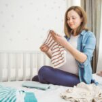 Pregnant woman nesting: folding baby's clothes/ laundry.