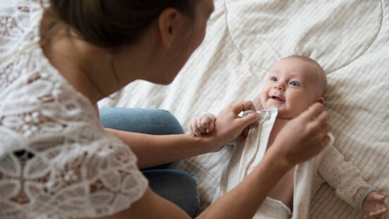 Mother dressing baby on bed