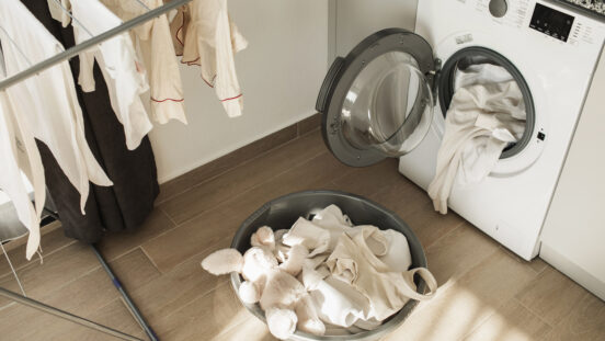 Laundry day on living room with washing machine, basket with clothes and drying clothesline. Modern kitchen with washing machine, dryer and laundry detergent. Laundry day. Routine home chores.