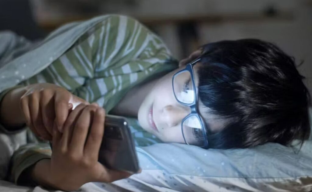 Teen boy laying in bed looking at social media on phone