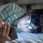 Teen boy laying in bed looking at social media on phone