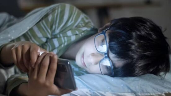 Teen boy laying in bed looking at social media on phone